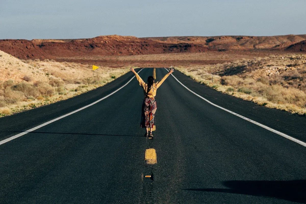 A lone woman in the middle of a desert road, her arms reaching for the sky