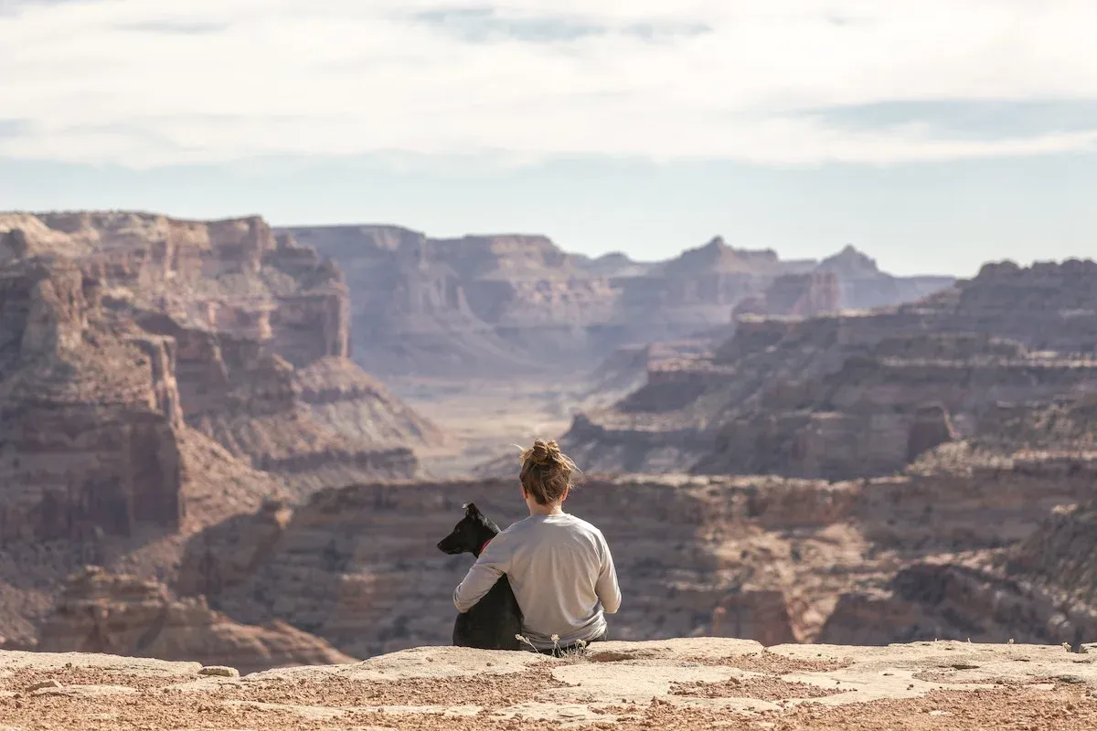 A lone woman on top of a cliff, facing a mountainous landscape