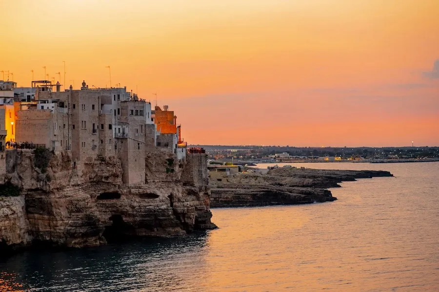 A sunset over buildings clinging to a cliff by the sea